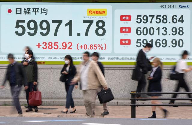 Pedestrians walk past an electronic quotation board displaying the Nikkei Stock Average on the Tokyo Stock Exchange along a street in Tokyo on April 23, 2026. Japan's Nikkei index soared above 60,000 points for the first time in early trade on April 23, as tech shares attracted buyers, while South Korea's Kospi also reached a new high. (Photo by Kazuhiro NOGI / AFP)