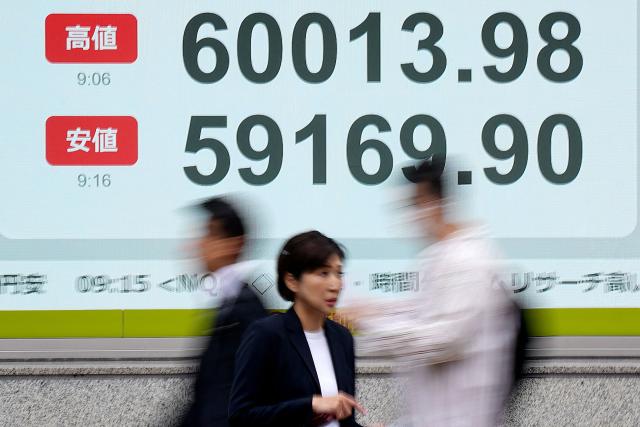 People walk past an electronic quotation board displaying the Nikkei Stock Average on the Tokyo Stock Exchange (top to bottom) highest price, and lowest price of the morning, along a street in Tokyo on April 23, 2026. Japan's Nikkei index soared above 60,000 points for the first time in early trade on April 23, as tech shares attracted buyers, while South Korea's Kospi also reached a new high. (Photo by Kazuhiro NOGI / AFP)