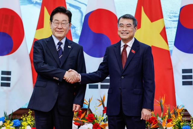 Vietnam's Prime Minister Le Minh Hung (R) and South Korea's President Lee Jae Myung (L) shake hands during a meeting at the Government Office in Hanoi on April 23, 2026. (Photo by LUONG THAI LINH / POOL / AFP)