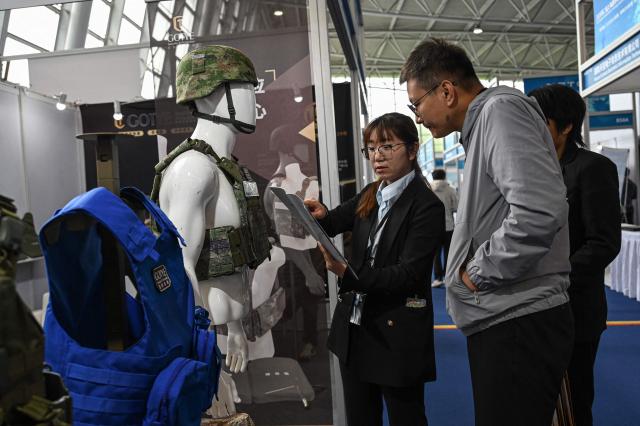 An exhibitor (C) introduces their security gear products at the National Defense Technology Industrial Equipment and Information Technology Expo in Shanghai on April 23, 2026. (Photo by Jade GAO / AFP)