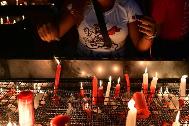 A woman lights a candle during Saint George's Day (Sao Jorge) celebrations at the Quintino neighborhood in Rio de Janeiro, Brazil on April 22, 2026. (Photo by Pablo PORCIUNCULA / AFP)