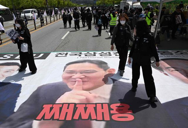 Members of the Samsung Electronics labour union walk on a banner showing a picture of Samsung Electronics Executive Chairman Lee Jae-yong as they stage a mass rally demanding the removal of a cap on performance bonuses, outside the company's foundry and semiconductor factory in Pyeongtaek on April 23, 2026. (Photo by Jung Yeon-je / AFP)