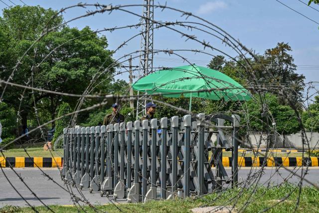 Security personnel keeping watch are seen through barbed wires at a closed road leading to the Serena Hotel in the Red Zone area of Islamabad on April 23, 2026. Pakistan's capital was still locked in gear on April 22 to host high-stakes US-Iran talks that were pushed back at the last minute overnight, but many residents began to tire of the heavy personal and economic toll of tight security restrictions. (Photo by Asif HASSAN / AFP)
