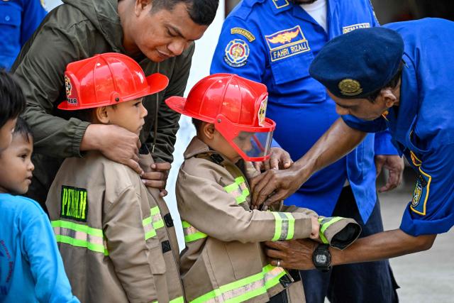 Firefighters prepare kindergarten students before teaching them how to use a water hose in Banda Aceh on April 23, 2026. (Photo by CHAIDEER MAHYUDDIN / AFP)