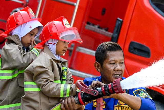 A firefighter teaches kindergarten students how to use a water hose in Banda Aceh on April 23, 2026. (Photo by CHAIDEER MAHYUDDIN / AFP)