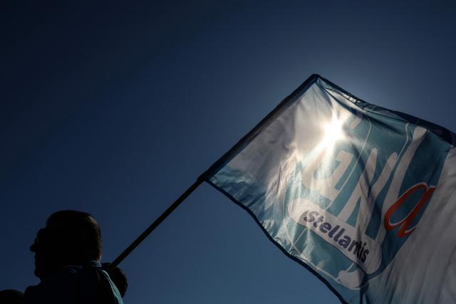 An employee of multinational automotive manufacturing corporation Stellantis holds a flag reading "Stellantis" during a demonstration called by trade unions outside the Poissy City Hall, in the outskirts of Paris, on April 23, 2026. The car manufacturer Stellantis announced on April 16, 2026 that it would cease car production at its historic Poissy plant after 2028, thereby turning a page in the industrial history of the Paris region. (Photo by Alain JOCARD / AFP)