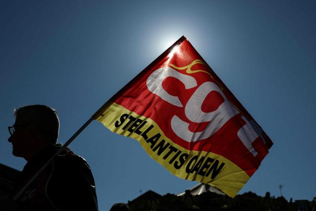 An employee of multinational automotive manufacturing corporation Stellantis holds a flag of French trade union General Confederation of Labour (CGT) reading "Stellantis" during a demonstration called by trade unions outside the Poissy City Hall, in the outskirts of Paris, on April 23, 2026. The car manufacturer Stellantis announced on April 16, 2026 that it would cease car production at its historic Poissy plant after 2028, thereby turning a page in the industrial history of the Paris region. (Photo by Alain JOCARD / AFP)