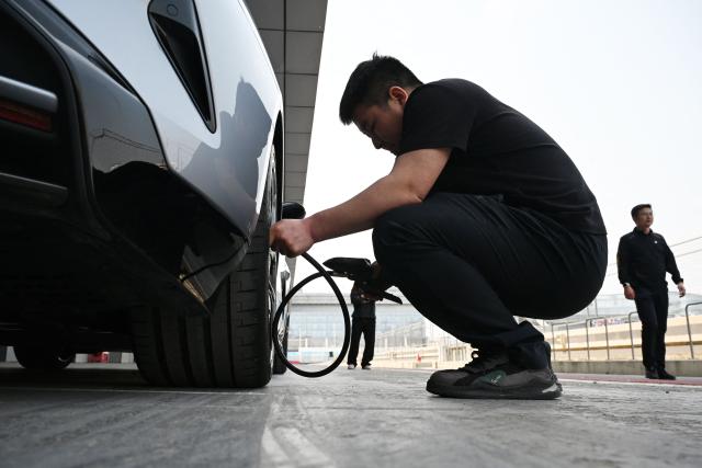 A technician checks tyre pressure on a Xiaomi SU7 Ultra during a Xiaomi track day driving experience in Tianjin, in northern China on April 23, 2026, ahead of the Beijing Auto Show which opens on April 24. (Photo by GREG BAKER / AFP)