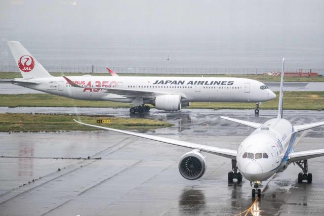 A Japan Airlines (JAL) Airbus A350-900 (L) and an All Nippon Airways (ANA) Boeing 787 passenger aircraft are seen from the observation area of Tokyo's Haneda Airport on April 23, 2026. (Photo by Philip FONG / AFP)