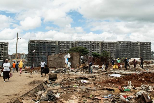 Residents of Soweto Zone D walk past the remains of demolished structures in front of buildings under construction for a state affordable housing programme following government-planned demolitions carried out to make space for the project at the Kibera informal settlement, in Nairobi on April 23, 2026. Kenyas Affordable Housing Programme is a government initiative to replace informal settlements with low-cost housing. In Kibera, the largest informal settlement in Kenya, demolitions have cleared some areas for new developments aimed at improving living conditions and home ownership. However, the programme has faced controversy over evictions, compensation and displacement of residents before completion of new housing. (Photo by Gordwin Odhiambo / AFP)
