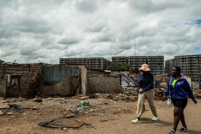 Residents of Soweto Zone D walk past the remains of demolished structures in front of buildings under construction for a state affordable housing programme following government-planned demolitions carried out to make space for the project at the Kibera informal settlement, in Nairobi on April 23, 2026. Kenyas Affordable Housing Programme is a government initiative to replace informal settlements with low-cost housing. In Kibera, the largest informal settlement in Kenya, demolitions have cleared some areas for new developments aimed at improving living conditions and home ownership. However, the programme has faced controversy over evictions, compensation and displacement of residents before completion of new housing. (Photo by Gordwin Odhiambo / AFP)