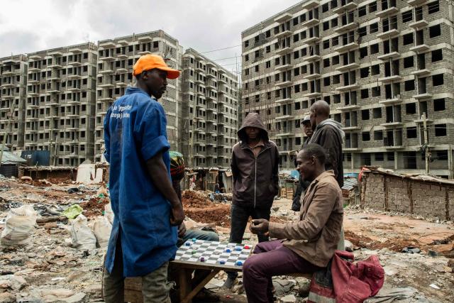 Residents of Soweto Zone D play checkers at the remains of demolished houses in front of buildings under construction for a state affordable housing programme following government-planned demolitions carried out to make space for the project at the Kibera informal settlement, in Nairobi on April 23, 2026. Kenyas Affordable Housing Programme is a government initiative to replace informal settlements with low-cost housing. In Kibera, the largest informal settlement in Kenya, demolitions have cleared some areas for new developments aimed at improving living conditions and home ownership. However, the programme has faced controversy over evictions, compensation and displacement of residents before completion of new housing. (Photo by Gordwin Odhiambo / AFP)