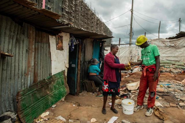 Kule Tosh, a resident of Soweto Zone D (R), receives a snack during a break from clearing land in front of buildings under construction for a state affordable housing programme following government-planned demolitions carried out to make space for the project at the Kibera informal settlement, in Nairobi on April 23, 2026. Kenyas Affordable Housing Programme is a government initiative to replace informal settlements with low-cost housing. In Kibera, the largest informal settlement in Kenya, demolitions have cleared some areas for new developments aimed at improving living conditions and home ownership. However, the programme has faced controversy over evictions, compensation and displacement of residents before completion of new housing. (Photo by Gordwin Odhiambo / AFP)