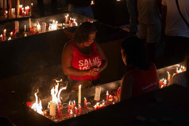 A woman lights a candle during Saint George's Day (Sao Jorge) celebrations at the Quintino neighborhood in Rio de Janeiro, Brazil on April 23, 2026. (Photo by Pablo PORCIUNCULA / AFP)