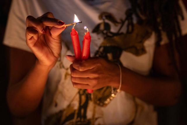 A woman lights a candle during Saint George's Day (Sao Jorge) celebrations at the Quintino neighborhood in Rio de Janeiro, Brazil on April 23, 2026. (Photo by Pablo PORCIUNCULA / AFP)