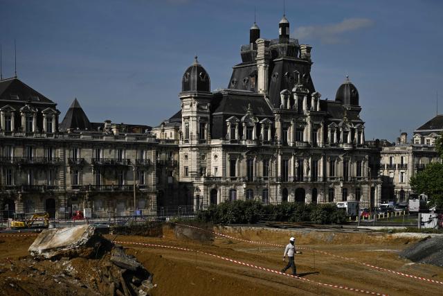 A worker crosses an excavation site in front of a preserved 19th-century building facade at the Canopia urban redevelopment site near the Saint-Jean railway station in Bordeaux, south-western France, on April 23, 2026. The city's redevelopment push comes as the European Central Bank warned that the Iran conflict risks pushing energy-dependent European economies into stagflation, with French construction firms reporting fuel and materials cost hikes across active sites. (Photo by Philippe LOPEZ / AFP)