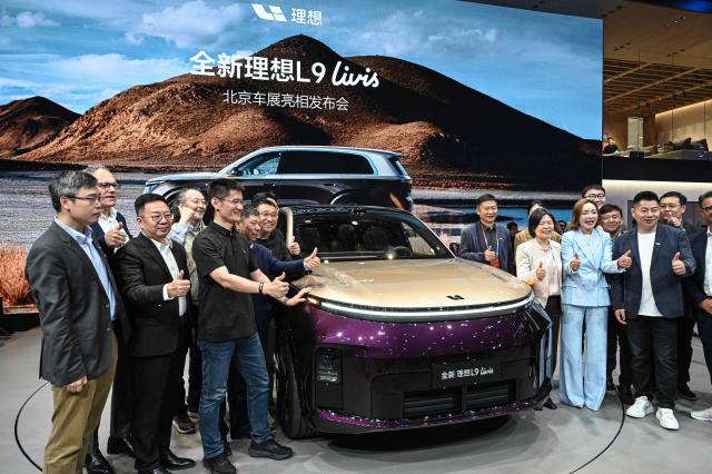 Employees of Li Auto take a group photo next to newly-launched L9 levis model car at the Beijing Auto Show in Beijing on April 24, 2026. (Photo by JADE GAO / AFP)