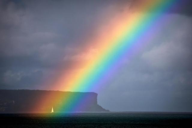 A sailing boat passes a rainbow in front of North Head on Sydney Harbour on April 24, 2026. (Photo by DAVID GRAY / AFP)