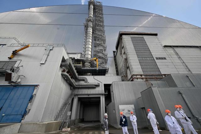 Employees stand in front of the New Safe Confinement (NSC), covering the destroyed fourth reactor at the Chernobyl Nuclear Power Plant on April 23, 2026. Ukraine will on April 26, 2026 mark the 40th anniversary of the Chernobyl accident, the worst civilian nuclear disaster in history. The risks of new radioactive releases still remain today, as the site is threatened by Russian strikes after it invaded the neighbour four years ago. (Photo by Sergei SUPINSKY / AFP)