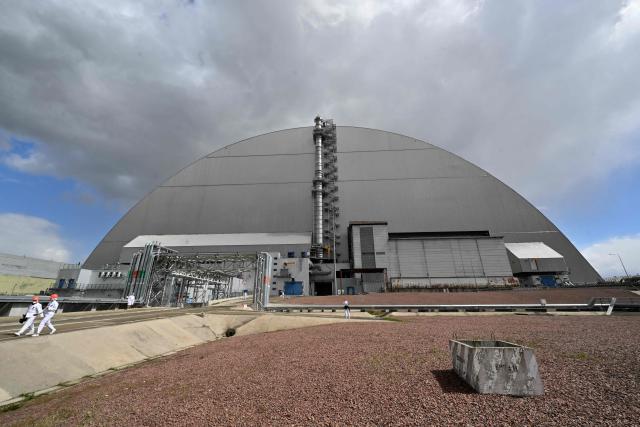 Employees walk in front of New Safe Confinement (NSC), covering the destroyed fourth reactor at the Chernobyl Nuclear Power Plant on April 23, 2026. Ukraine will on April 26, 2026 mark the 40th anniversary of the Chernobyl accident, the worst civilian nuclear disaster in history. The risks of new radioactive releases still remain today, as the site is threatened by Russian strikes after it invaded the neighbour four years ago. (Photo by Sergei SUPINSKY / AFP)