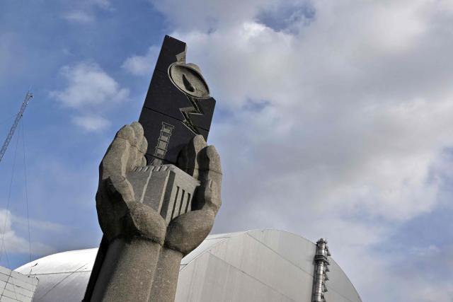 This photograph shows the monument in memory of the victims of the Chernobyl nuclear disaster in front of New Safe Confinement (NSC), covering the destroyed fourth reactor at the Chernobyl Nuclear Power Plant on April 23, 2026. Ukraine will on April 26, 2026 mark the 40th anniversary of the Chernobyl accident, the worst civilian nuclear disaster in history. The risks of new radioactive releases still remain today, as the site is threatened by Russian strikes after it invaded the neighbour four years ago. (Photo by Sergei SUPINSKY / AFP)