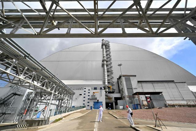 Employees stand in front of New Safe Confinement (NSC), covering the destroyed fourth reactor at the Chernobyl Nuclear Power Plant on April 23, 2026. Ukraine will on April 26, 2026 mark the 40th anniversary of the Chernobyl accident, the worst civilian nuclear disaster in history. The risks of new radioactive releases still remain today, as the site is threatened by Russian strikes after it invaded the neighbour four years ago. (Photo by Sergei SUPINSKY / AFP)