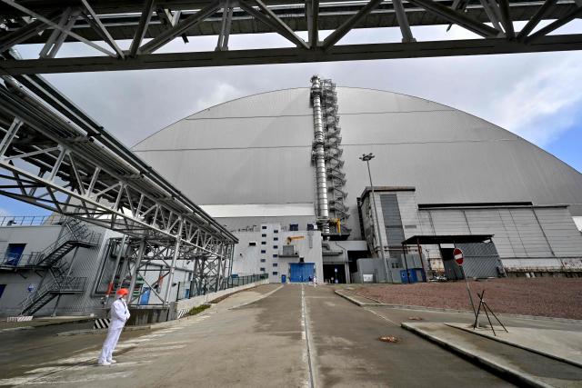 An employee stands in front of the New Safe Confinement (NSC), covering the destroyed fourth reactor at the Chernobyl Nuclear Power Plant on April 23, 2026. Ukraine will on April 26, 2026 mark the 40th anniversary of the Chernobyl accident, the worst civilian nuclear disaster in history. The risks of new radioactive releases still remain today, as the site is threatened by Russian strikes after it invaded the neighbour four years ago. (Photo by Sergei SUPINSKY / AFP)