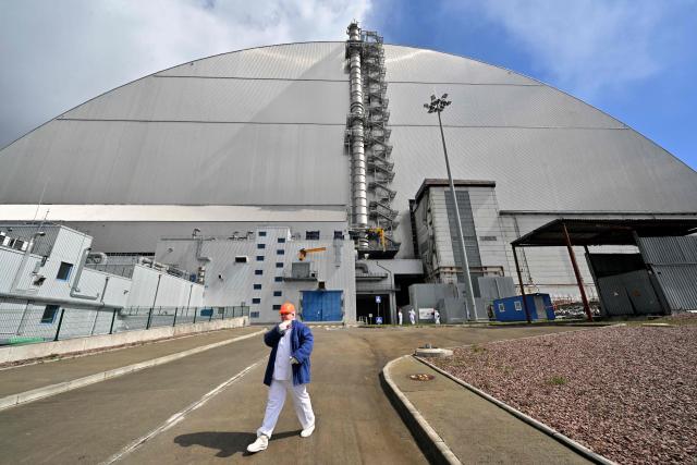TOPSHOT - An employee walks past the New Safe Confinement (NSC), covering the destroyed fourth reactor at the Chernobyl Nuclear Power Plant on April 23, 2026. Ukraine will on April 26, 2026 mark the 40th anniversary of the Chernobyl accident, the worst civilian nuclear disaster in history. The risks of new radioactive releases still remain today, as the site is threatened by Russian strikes after it invaded the neighbour four years ago. (Photo by Sergei SUPINSKY / AFP)