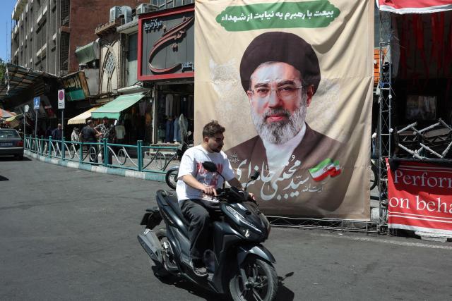 An man rides his motorcycle past a billboard depicting Iran's Supreme Leader Ayatollah Mojtaba Khamenei, in Tehran on April 24, 2026. (Photo by AFP) / 