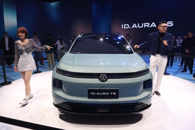 Hosts speak in front of a Volkswagen ID AURA T6 on the opening day of the Beijing Auto Show in Beijing on April 24, 2026. (Photo by CN-STR / AFP) / China OUT