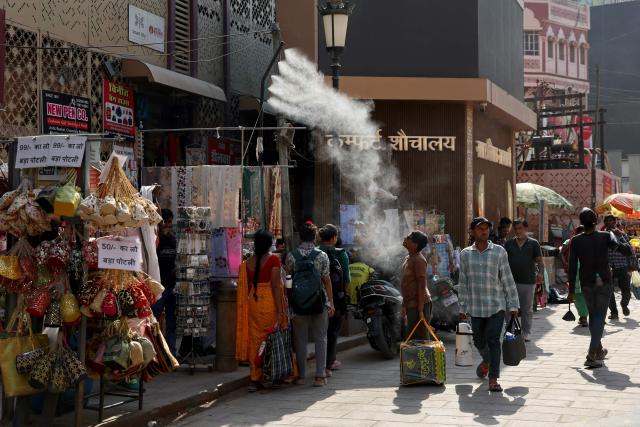 A boy stands beneath a water sprinkler mounted on a pole along a street on a hot summer day in Varanasi on April 24, 2026. Summer heat in the world's most populous nation can be brutal -- putting millions of people at risk, with nearly 11,000 people dying due to heat stroke between 2012 and 2021, according to government data. (Photo by Niharika KULKARNI / AFP)