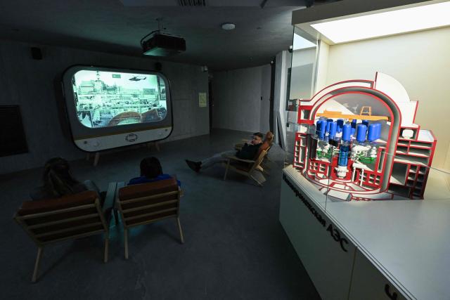 People watch a documentary about Chernobyl tragedy at a temporary display dedicated to the 40th anniversary of the explosion at the Chernobyl nuclear power plant - the worst civilian nuclear disaster in history, at the Atom pavilion, a permanent exhibition centre designed to demonstrate Russia's main past and modern achievements of the nuclear power industry, at the All-Russia Exhibition Centre (VDNH) in Moscow on April 24, 2026. (Photo by Igor IVANKO / AFP)