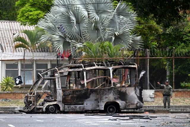 A Colombian officer gestures next to a bus bomb after an explosion near a military base in Cali, Valle del Cauca department, Colombia taken on April 24, 2026. One person was injured in an attack on a military base in southwest Colombia on April 24, 2026, according to the local health authority, one month ahead of the presidential election. (Photo by JOAQUIN SARMIENTO / AFP)