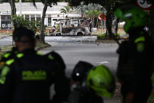 Colombian police officers stand next to a bus bomb after an explosion near a military base in Cali, Valle del Cauca department, Colombia taken on April 24, 2026. One person was injured in an attack on a military base in southwest Colombia on April 24, 2026, according to the local health authority, one month ahead of the presidential election. (Photo by JOAQUIN SARMIENTO / AFP)