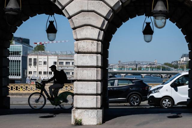A cyclist rides crossing the Bercy bridge from the northern bank (rive droite) to the southern bank (rive gauche) under a aerial metro railway with a view of the Seine river and motorised vehicles, in eastern Paris, on April 24, 2026. (Photo by Martin LELIEVRE / AFP)