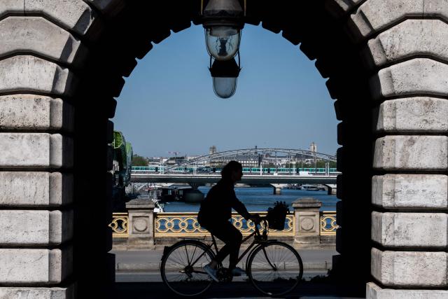A cyclist rides crossing the Bercy bridge from the southern bank (rive gauche) to the northern bank (rive droite) under a aerial metro railway with a view of the Seine river, in eastern Paris on April 24, 2026. (Photo by Martin LELIEVRE / AFP)