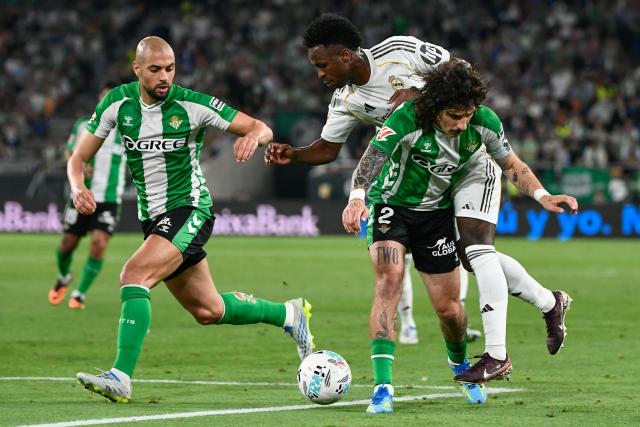 Real Madrid's Brazilian forward #07 Vinicius Junior (C) vies for the ball with Real Betis' Spanish defender #02 Hector Bellerin (R) and Real Betis' Moroccan midfielder #14 Sofyan Amrabat during the Spanish league football match between Real Betis and Real Madrid CF at the La Cartuja stadium in Seville on April 24 , 2026. (Photo by CRISTINA QUICLER / AFP)