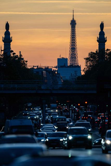 This photograph shows motorised vehicles in traffic with a view of the Eiffel tower at sunset, near Porte de Vincennes, in Paris on April 24, 2026. (Photo by Martin LELIEVRE / AFP)