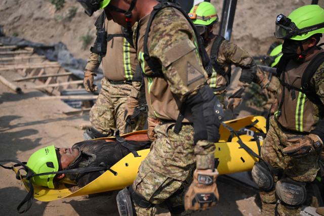 Salvadoran soldiers carry a man during a post-earthquake rescue simulation in the final phase of a 36 hour emergency exercise, held as part of the CENTAM Guardian 2026 military drills, at the Engineers Corps (CIFA) facilities in San Juan Opico, El Salvador, on April 24, 2026. (Photo by Marvin RECINOS / AFP)