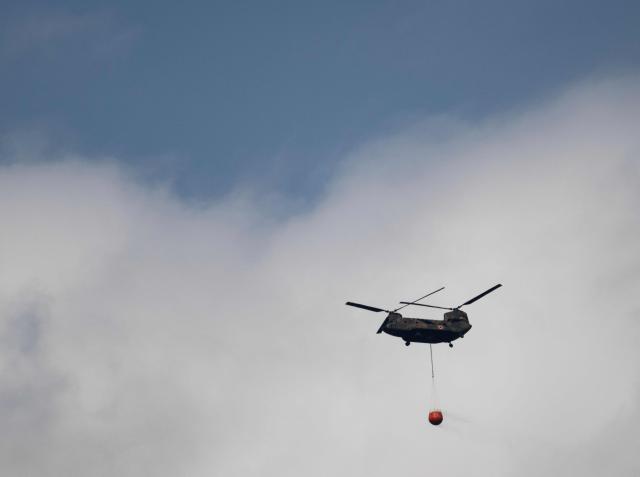 A helicopter doing water drops flies over smoke from a forest fire near the town of Otsuchi, in Iwate Prefecture on April 25, 2026. (Photo by ANDREW CABALLERO-REYNOLDS / AFP)