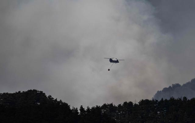 A helicopter doing water drops flies over smoke from a forest fire near the town of Otsuchi, in Iwate Prefecture on April 25, 2026. (Photo by ANDREW CABALLERO-REYNOLDS / AFP)
