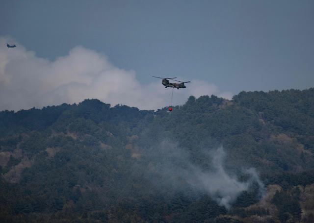 Two helicopters doing water drops fly over smoke from a forest fire on the side of a hill side near the town of Otsuchi, in Iwate Prefecture on April 25, 2026. (Photo by ANDREW CABALLERO-REYNOLDS / AFP)