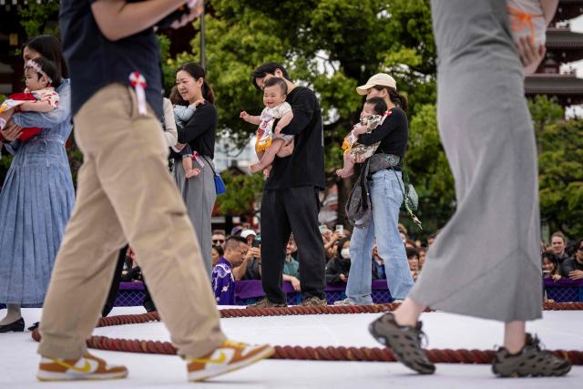 Parents hold their child before the start of the "crying baby sumo" match at the Sensoji temple in Tokyo on April 25, 2026. Japanese parents believe that sumo wrestlers can help make babies cry out a wish to grow up with good health. (Photo by Yuichi YAMAZAKI / AFP)