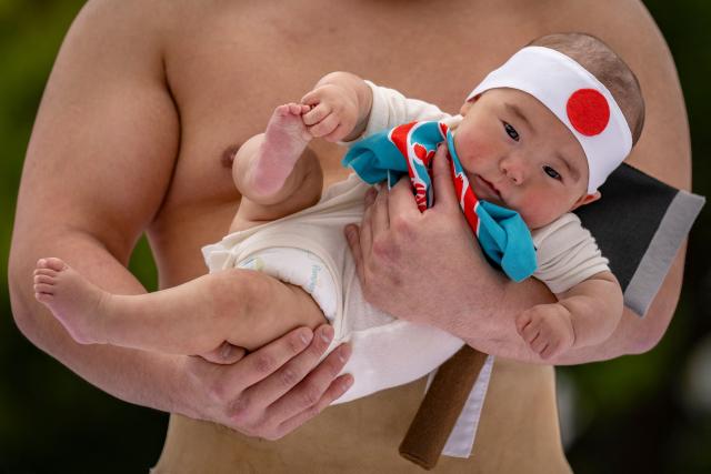 A sumo wrestler holds a child during the "crying baby sumo" match at Sensoji temple in Tokyo on April 25, 2026. Japanese parents believe that sumo wrestlers can help make babies cry out a wish to grow up with good health. (Photo by Yuichi YAMAZAKI / AFP)