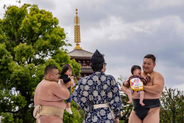 Sumo wrestlers hold children during their "crying baby sumo" match at Sensoji temple in Tokyo on April 25, 2026. Japanese parents believe that sumo wrestlers can help make babies cry out a wish to grow up with good health. (Photo by Yuichi YAMAZAKI / AFP)