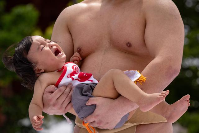A sumo wrestler holds a child during the "crying baby sumo" match at Sensoji temple in Tokyo on April 25, 2026. Japanese parents believe that sumo wrestlers can help make babies cry out a wish to grow up with good health. (Photo by Yuichi YAMAZAKI / AFP)