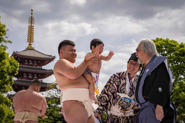 Sumo wrestlers hold children during their "crying baby sumo" match at Sensoji temple in Tokyo on April 25, 2026. Japanese parents believe that sumo wrestlers can help make babies cry out a wish to grow up with good health. (Photo by Yuichi YAMAZAKI / AFP)