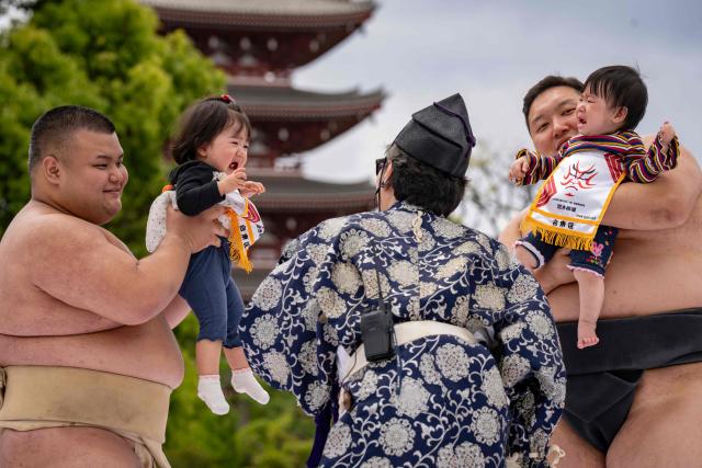 Sumo wrestlers hold children during their "crying baby sumo" match at Sensoji temple in Tokyo on April 25, 2026. Japanese parents believe that sumo wrestlers can help make babies cry out a wish to grow up with good health. (Photo by Yuichi YAMAZAKI / AFP)