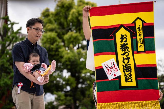 A parents holds his child before the start of the "crying baby sumo" match at the Sensoji temple in Tokyo on April 25, 2026. Japanese parents believe that sumo wrestlers can help make babies cry out a wish to grow up with good health. (Photo by Yuichi YAMAZAKI / AFP)