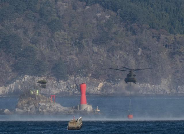 A Japan Self Defense Force helicopter reloads with a payload of water from the bay as a forest fire burns around the town of Otsuchi in Iwate Prefecture on April 25, 2026. Hundreds of firefighters were battling wildfires in the forests of northern Japan on April 25, as authorities urged more than 3,200 people to evacuate from their homes, government officials said. (Photo by ANDREW CABALLERO-REYNOLDS / AFP)